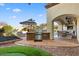 Outdoor kitchen and patio area with a built-in grill, seating, and serene views of the landscaped backyard at 6960 E Ivyglen St, Mesa, AZ 85207