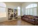 Bright living room featuring built-in bookshelves, arched windows, plantation shutters and a brown leather sofa at 7415 W Via De Luna Dr, Glendale, AZ 85310