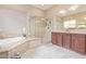 Bright bathroom featuring dual sinks, a soaking tub, walk-in shower, and elegant marble tiling at 30056 N 129Th Ave, Peoria, AZ 85383