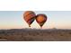 Two hot air balloons in flight over a desert landscape with mountains in the distance at 31489 N 126Th Ln, Peoria, AZ 85383