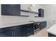 Modern kitchen featuring sleek navy cabinets, stainless steel appliances, and a stylish white backsplash at 550 E Aurora Dr, San Tan Valley, AZ 85140