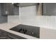 Close-up of induction cooktop with white geometrical backsplash and gray cabinetry at 42855 W Palo Abeto Dr, Maricopa, AZ 85138