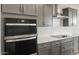 Stainless steel oven and range hood with white geometrical backsplash and gray cabinets at 42855 W Palo Abeto Dr, Maricopa, AZ 85138