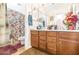 Bathroom features a double vanity, wood cabinets and a shower with floral curtain at 8615 S 45Th Gln, Laveen, AZ 85339