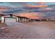 Single-story home featuring a two-car garage and large dirt lot under a vibrant sunset sky at 20438 W Carver Rd, Buckeye, AZ 85326