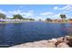 Tranquil community pond surrounded by trees and greenery under a bright blue sky with fluffy clouds at 37093 W La Paz St, Maricopa, AZ 85138