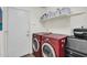 Bright laundry room with red washer and dryer units, shelving, white walls, and a door to the outside at 9652 E Ludlow Dr, Scottsdale, AZ 85260