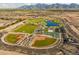 Wide aerial shot highlighting community amenities: baseball fields, tennis courts, a pond, and walking paths with mountain views at 12551 W Parkway Ln, Avondale, AZ 85323