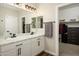 Bathroom featuring double sinks, white cabinets, and a view into a walk-in closet with shelving at 17618 W Paraiso Dr, Surprise, AZ 85387