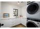 Bright laundry room featuring stacked washer and dryer, white cabinets and a view to the outdoors at 22619 N La Senda Dr, Scottsdale, AZ 85255