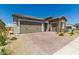 View of the front exterior, showing a three car garage, desert landscaping, and brick paved driveway at 27366 W Escuda Dr, Buckeye, AZ 85396