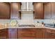 Close up view of the kitchen with dark wood cabinets, granite counters, and herringbone backsplash behind cooktop at 7717 W Noble Prairie Way, Florence, AZ 85132