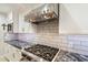 Close-up of stainless steel gas range cooktop and hood over granite counters and tile backsplash at 6803 E Main St # 2210, Scottsdale, AZ 85251