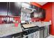 Modern kitchen with stainless steel appliances, granite countertops, dark cabinets and red accent wall at 3482 N 300Th Dr, Buckeye, AZ 85396