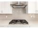 Close up on a modern cooktop with stainless steel vent hood and tiled backsplash at 21960 E Saddle Ct, Queen Creek, AZ 85142