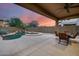 Covered patio with outdoor dining area overlooking a sparkling pool and desert landscape at dusk at 3419 W Thoreau Ln, Anthem, AZ 85086