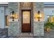 Close-up of a stone-clad entryway with a solid wood door and decorative lantern-style sconces at 8713 N 80Th Pl, Scottsdale, AZ 85258