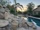 Backyard pool featuring rock waterfall, palm trees, lounge chairs, and beautiful desert sunset views at 7100 E Montgomery Rd, Scottsdale, AZ 85266