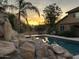 Inviting pool area at sunset with rock waterfall feature and desert landscaping at 7100 E Montgomery Rd, Scottsdale, AZ 85266