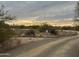 Desert property entrance with a gravel driveway, natural vegetation, and a distant view of the sunset at 7100 E Montgomery Rd, Scottsdale, AZ 85266