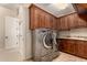 Well-lit laundry room featuring wood cabinetry, granite countertops, and stainless steel washer and dryer at 9955 E Celtic Dr, Scottsdale, AZ 85260