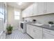 Bright laundry room featuring modern washer, dryer, sink, white cabinets, and decorative patterned floor at 15683 W Mercer Ln, Surprise, AZ 85379