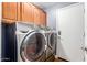 Laundry room with modern washer and dryer set under wood cabinets, adjacent to a white door at 5356 W Jupiter Way, Chandler, AZ 85226