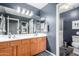 Well-lit bathroom with dual sinks, wood cabinets, large mirrors, and blue walls with a stylish rug at 12162 W Dreyfus Dr, El Mirage, AZ 85335