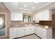 This kitchen features white cabinets, tile backsplash, neutral countertops and a stainless steel dishwasher at 12418 W Galaxy Dr, Sun City West, AZ 85375