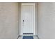 View of the front door, a white door surrounded by light taupe stucco walls and a black door mat at 16036 W Desert Hollow Dr, Surprise, AZ 85387