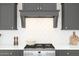 Close-up of kitchen range with gray cabinets, white backsplash, and sleek range hood at 20334 W Roma Ave, Buckeye, AZ 85396