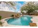 Backyard pool area with a rock waterfall feature, basketball hoop, and surrounding greenery at 7829 E Softwind Dr, Scottsdale, AZ 85255