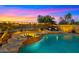 Inviting pool and spa featuring a waterfall, lounge chairs, lush landscaping, and beautiful sunset views at 3400 E Isaiah Ave, Gilbert, AZ 85298