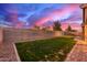 Backyard featuring green grass, gravel border, and a block fence with pink and purple sky at 3768 S Coach House Dr, Gilbert, AZ 85297