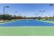 Well-maintained tennis court with vibrant blue and green surface, surrounded by fencing and lighting for evening play at 42906 W Darter Dr, Maricopa, AZ 85138