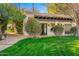Charming exterior featuring a covered porch with tiled roof, a lush lawn, and mature trees and bushes at 4900 E Desert Fairways Dr, Paradise Valley, AZ 85253