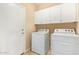 Functional laundry room with white appliances and upper cabinets for storage and a white door at 17846 W Fairview St, Goodyear, AZ 85338