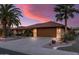 Charming house with desert landscaping and mature palm trees under a dramatic sunset and a spacious driveway at 20639 N 123Rd Dr, Sun City West, AZ 85375