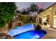 Dusk view of backyard pool and spa featuring rock waterfall and outdoor lighting at 3603 E Indigo Bay Ct, Gilbert, AZ 85234