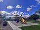 Community playground featuring a bright yellow slide, climbing equipment, and picnic tables under a blue, cloudy sky at 1735 W Wildwood Dr, Phoenix, AZ 85045