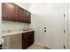 A laundry room featuring dark wood cabinets, granite counters, a stainless steel sink, and tile flooring at 2448 E Amber Ct, Gilbert, AZ 85296