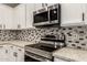 Modern kitchen featuring stainless steel appliances, white cabinetry, mosaic backsplash, and stone countertops at 20358 N Valencia N Dr, Maricopa, AZ 85138