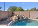 Resort-style backyard featuring a pool with stone accents, mature trees, and lush desert landscaping at 9237 W Alex Ave, Peoria, AZ 85382