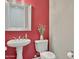 Stylish half bathroom with vibrant red walls, pedestal sink, and decorative mirror at 15829 W Bonitos Dr, Goodyear, AZ 85395