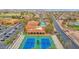 Aerial view of community with blue tennis courts, clubhouse, pool, palm trees, and surrounding desert landscape at 16215 W Indianola Ave, Goodyear, AZ 85395
