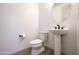 Clean powder room with a pedestal sink, round mirror, and modern toilet and fixtures at 16868 W Earll Dr, Goodyear, AZ 85395