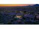 Aerial view of a vibrant community with homes featuring pools, desert landscaping, and city lights in the distance at 10999 E Acoma Dr, Scottsdale, AZ 85255