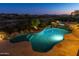 Gorgeous pool with spa framed by stone features, a patio, and views of the surrounding desert landscape and city lights at 10999 E Acoma Dr, Scottsdale, AZ 85255