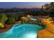 Backyard pool with rock waterfall and nearby dining table under an umbrella with views of the city at night at 10999 E Acoma Dr, Scottsdale, AZ 85255