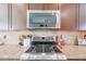 Close up of stainless steel microwave and gas range with granite countertops and tile backsplash at 16712 S 175Th Ln, Goodyear, AZ 85338